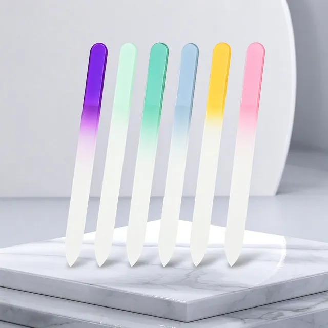 Seven gradient-coloured glass nail files standing on a white marble slab against a pink background