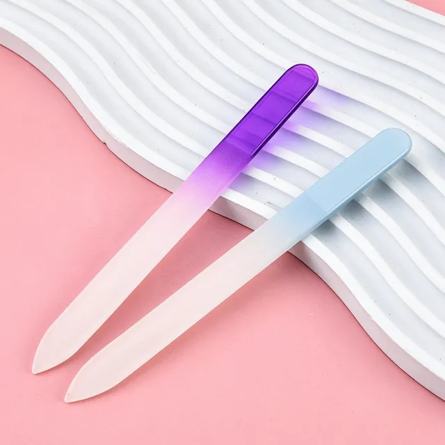 Two gradient glass nail files resting on a white wave-pattern plinth