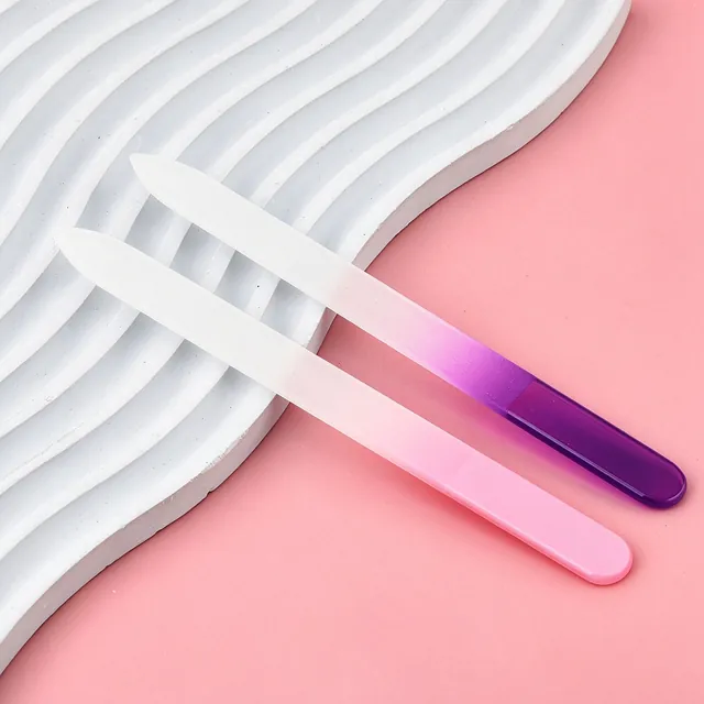 A clear and a purple gradient glass nail file crossed on a pink background