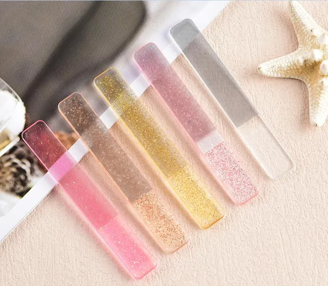 Five glitter glass nail files laid in a row on a linen cloth beside a starfish