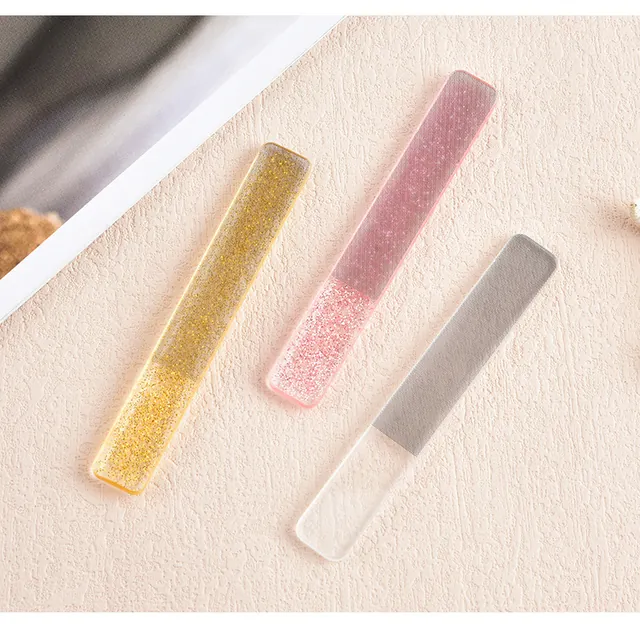 Three glitter glass nail files in gold, pink and grey on a linen cloth