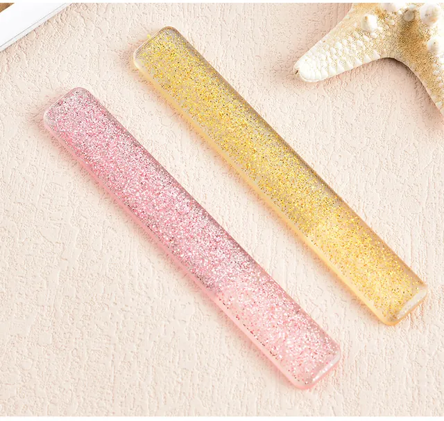 A pink and a gold glitter glass nail file resting on a linen cloth