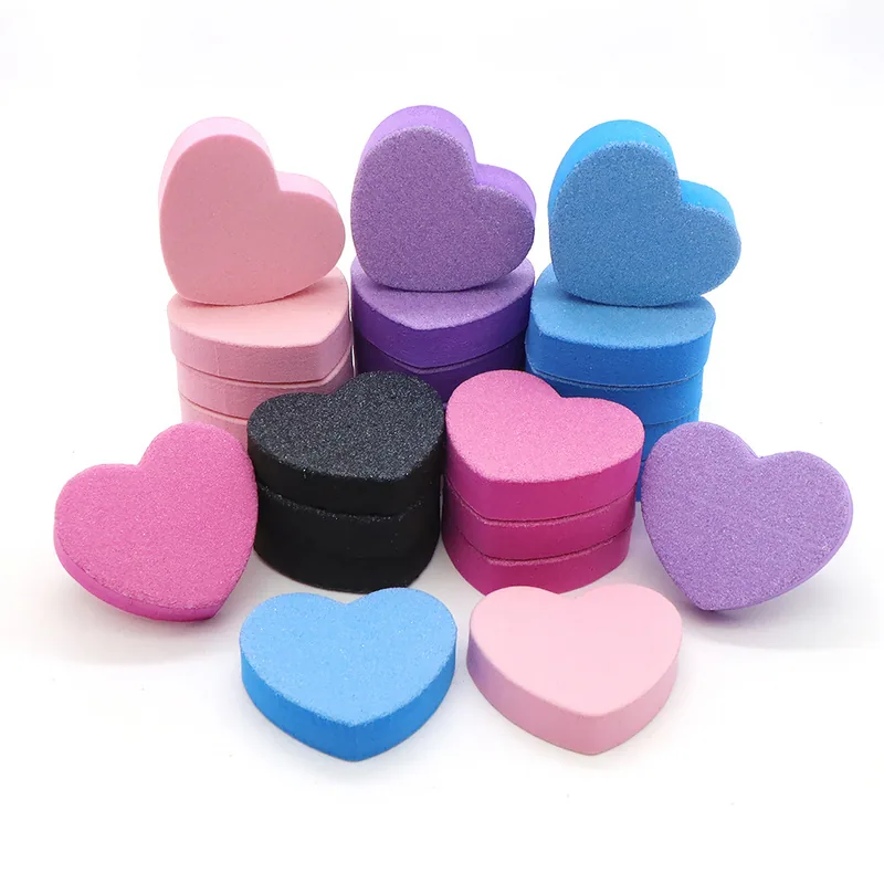 Mini heart-shaped sponge buffer blocks in pink, purple, blue and black piled on a white background